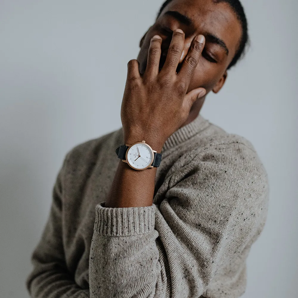 Eyes closed, a hand across the face, a rose gold Aspect on navy leather