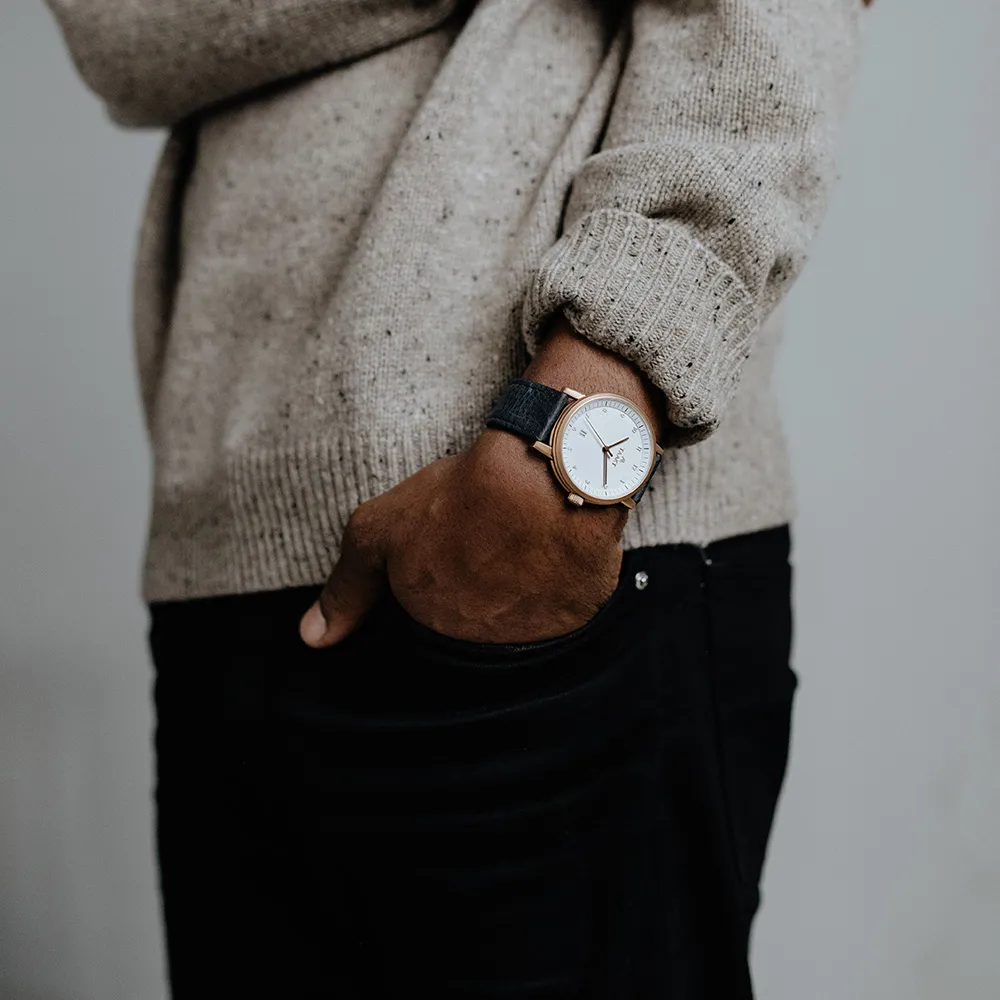 A hand in the pocket of black trousers, a rose gold Aspect on navy leather