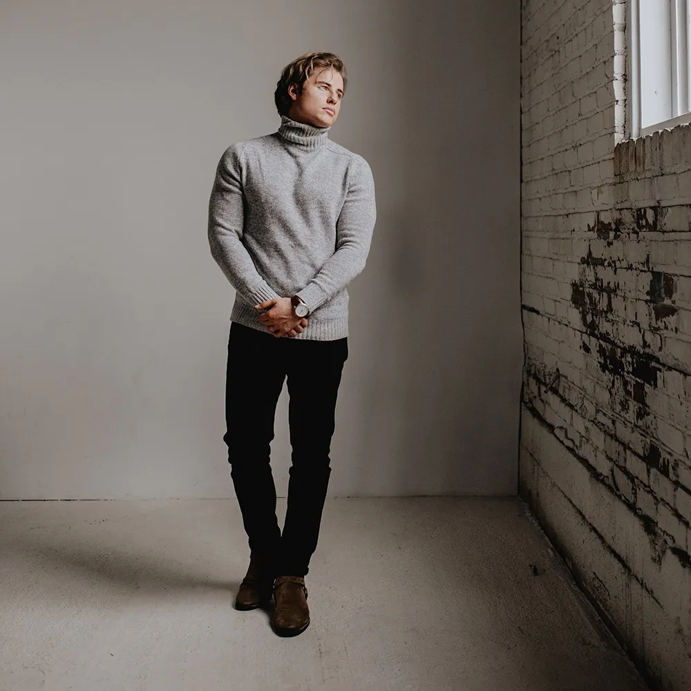 Standing in a whitewashed brick room in a gray turtleneck, a silver Aspect on brown leather