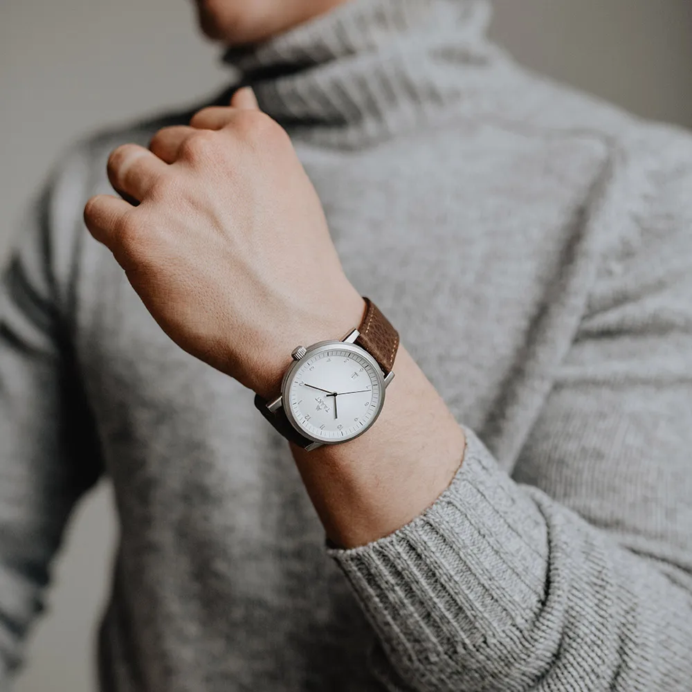 A silver Aspect on brown leather, against a gray turtleneck